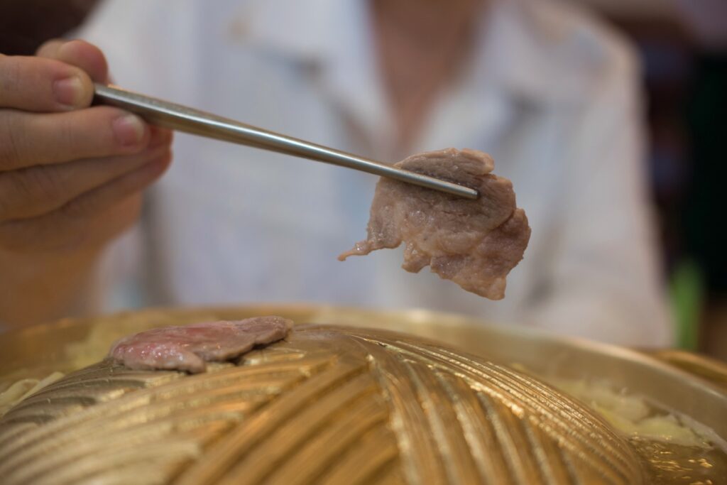 hand using steel chopsticks holding grilled pork slice on korean