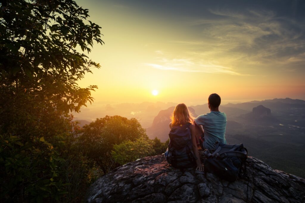 Two hikers on top of the mountain enjoying sunrise over the tropical valley