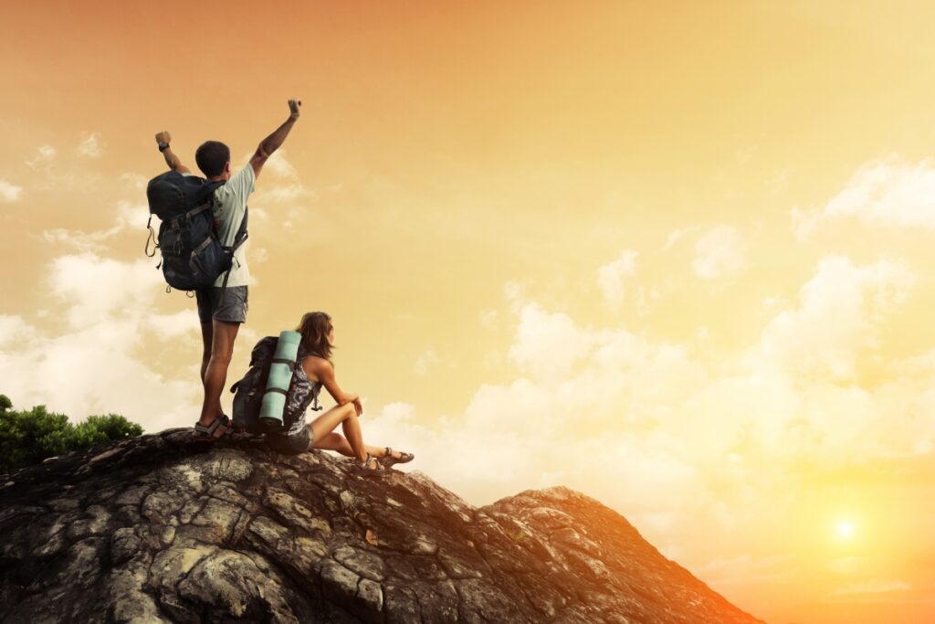 Two hikers with backpacks enjoying sunset view from top of a mountain