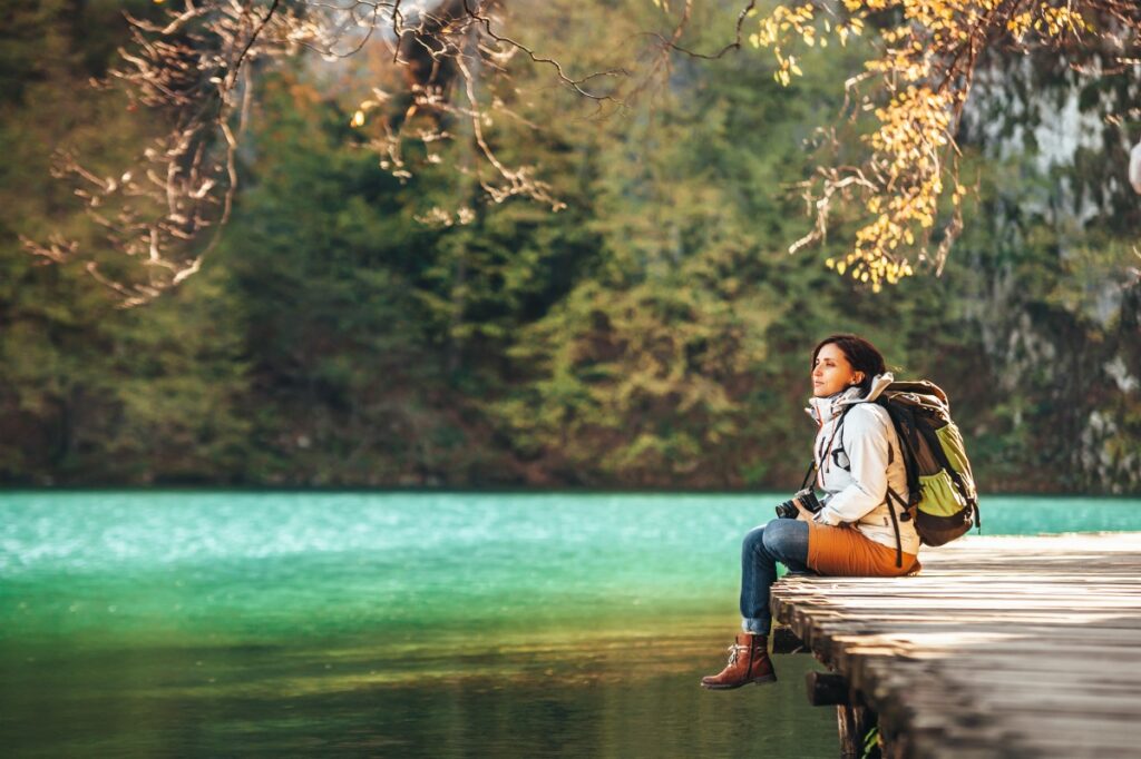 Woman traveler sits on wood bridge on mountain lake at sunny autumn day