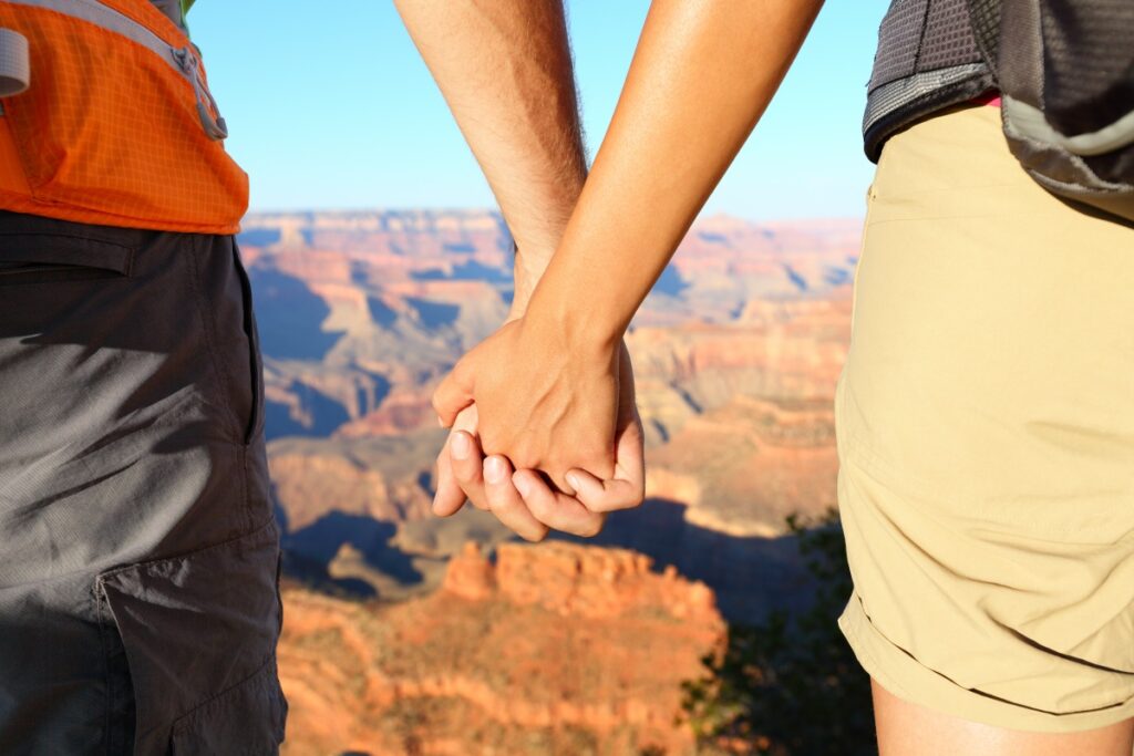 Romantic hiking couple holding hands, Grand Canyon. Close up of young lovers on hike enjoying view and romance. Woman and man hikers.