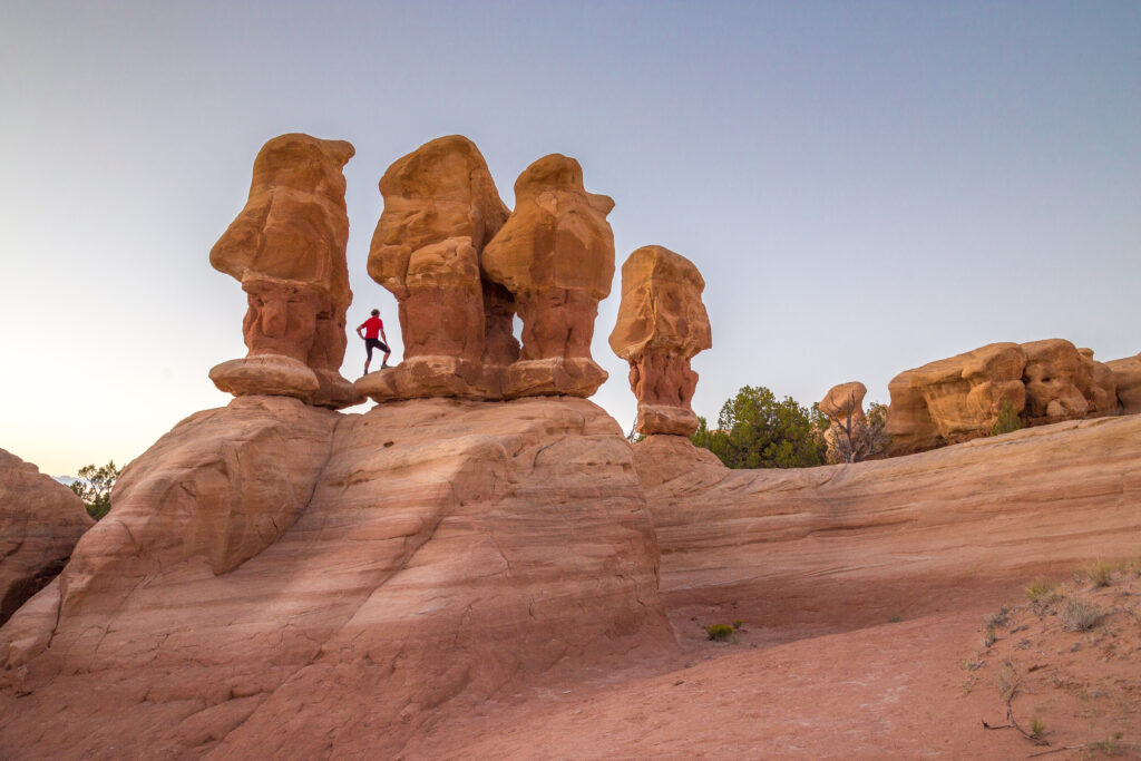 Beautiful view of male hiker standing between amazing Four Hoodoos sandstone formations in Devil's Garden in beautiful evening light at sunset, Grand Staircase-Escalante National Monument, Utah, USA