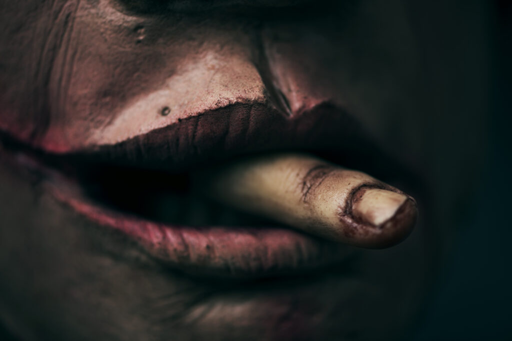closeup of a scary disfigured man with a bloody amputated finger emerging from his mouth