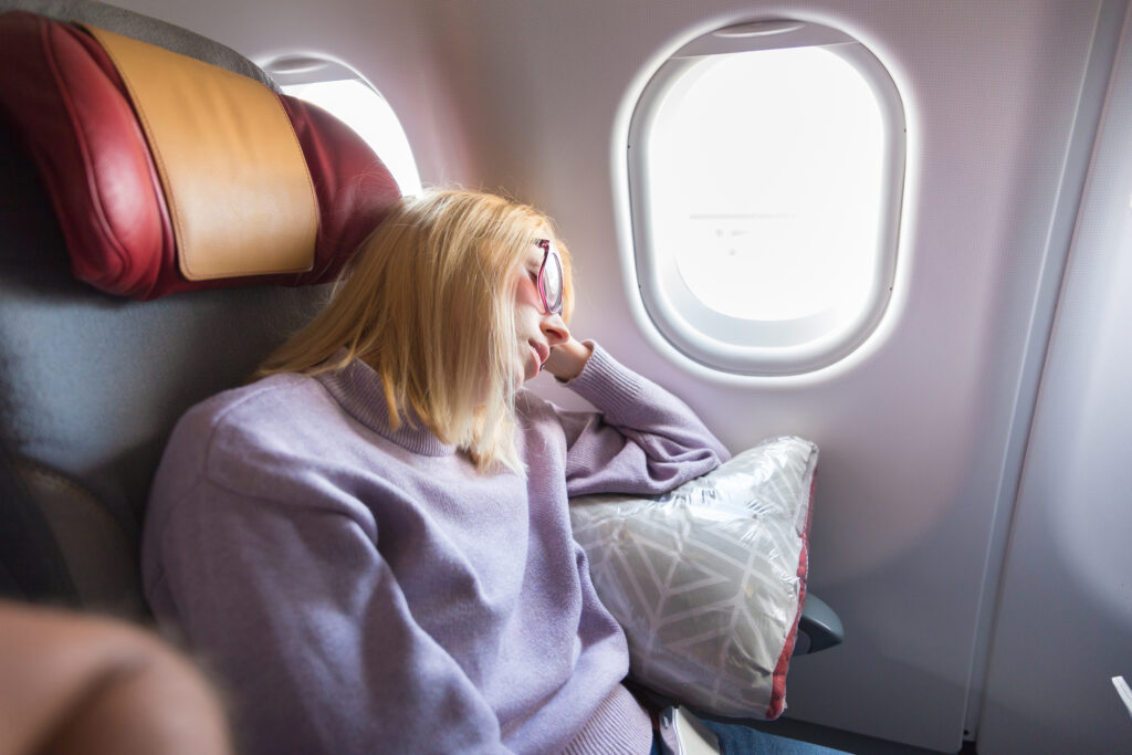 Tired blonde casual caucasian woman sleeping on seat while traveling by airplane on long distance transatlantic flight. Commercial transportation by planes.