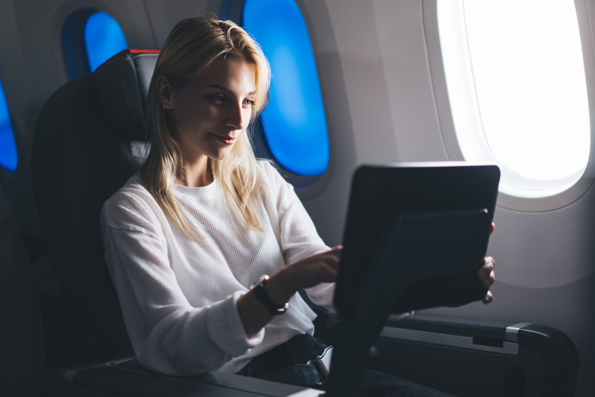 Lovely Caucasian girl passenger touching a handy LCD screen while selecting entertainment during a relaxing flight.  Play games, shop shopping, personal TV and movie selection on board