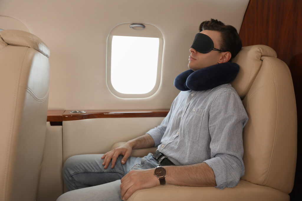 A young man wearing a travel pillow and mask sleeps on the plane during the flight