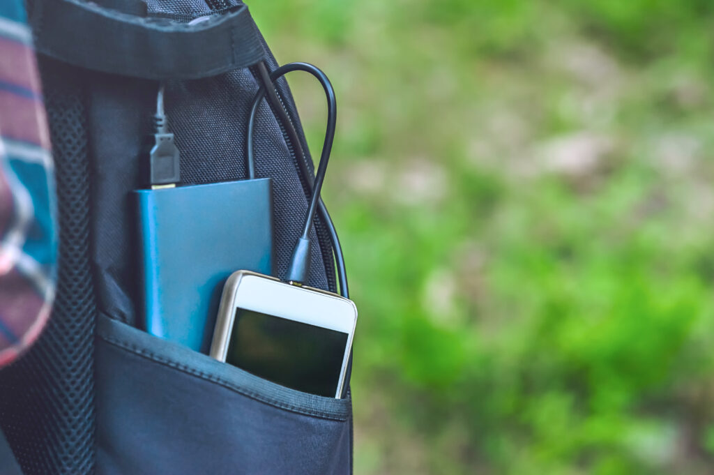 A power bank is charging a smartphone in a black backpack pocket, against a grass background