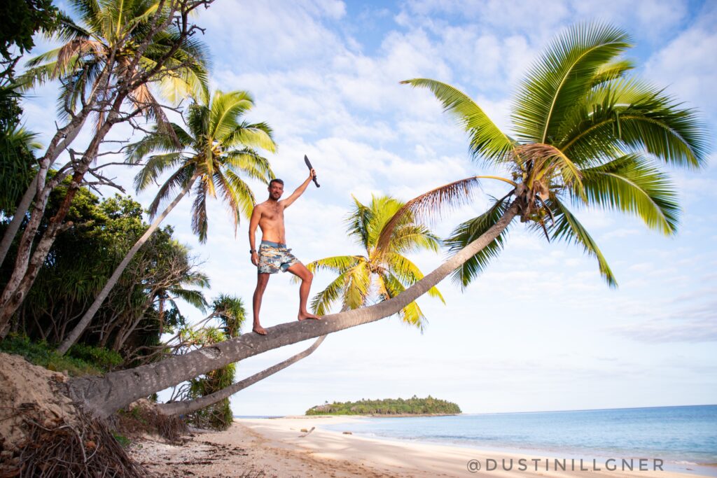 Tom Williams owner of Desert Island Survival on a palm tree with a knife