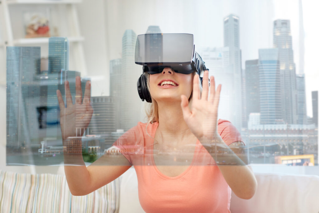 technology, augmented reality and entertainment concept - happy young woman in virtual headset 3d glasses and headphones playing game at home with singapore city skyscrapers on screen projection
