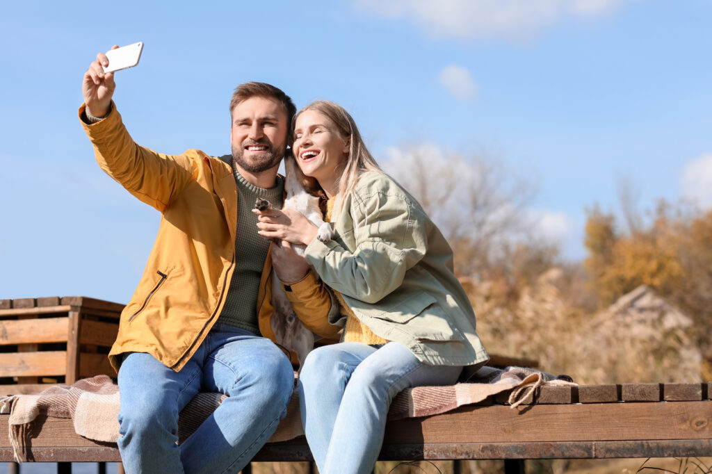 Lovely couple with cute dog taking selfie on autumn day