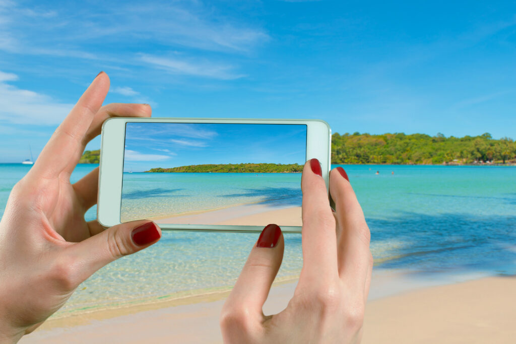 Summer, Travel, Vacation and Holiday concept - Back view of a woman taking photograph with a smart phone camera at the horizon on the beach