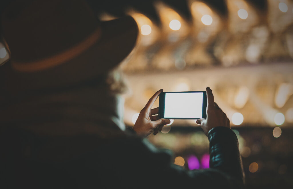 Closeup view from the back of a woman taking photo by a smartphone with a blank copy space display for your text message or advertising content. Horizontal, blurred background, bokeh effects.