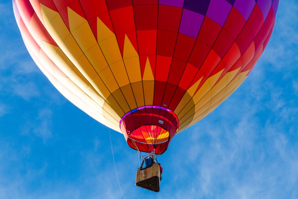 Brightly colored hot air balloon against blue morning sky just after take off